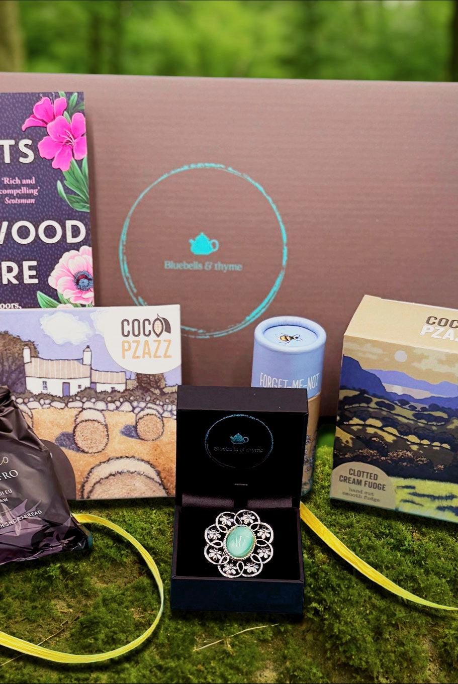 Summer meadow setting for Bluebells & Thyme 'Just Because' gift box with brooch, book, treats.