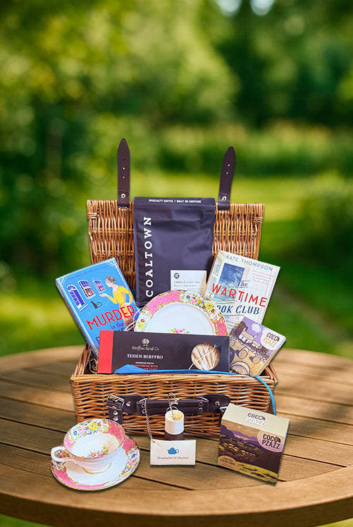 Garden table with Bluebells & Thyme 'Coffee & Serenity' hamper: vintage tea set, books, bookmarks, and Welsh treats.