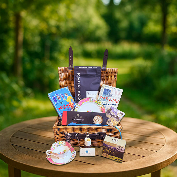 Garden table with Bluebells & Thyme 'Coffee & Serenity' hamper: vintage tea set, books, bookmarks, and Welsh treats.