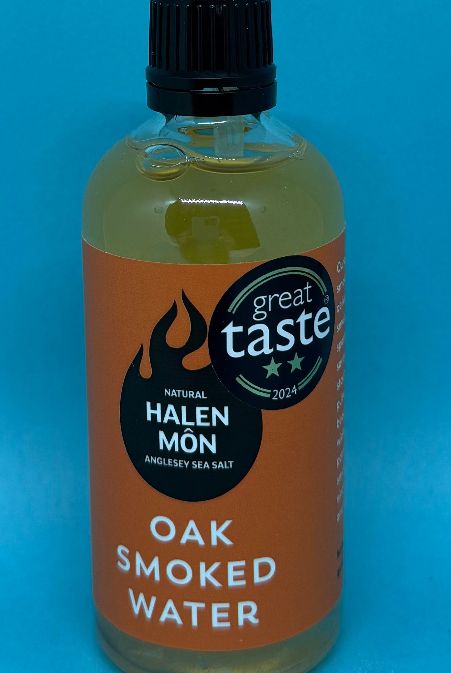 Bluebells and Thyme Bottle of Oak Smoked Water with Halen Mon label on a blue background
