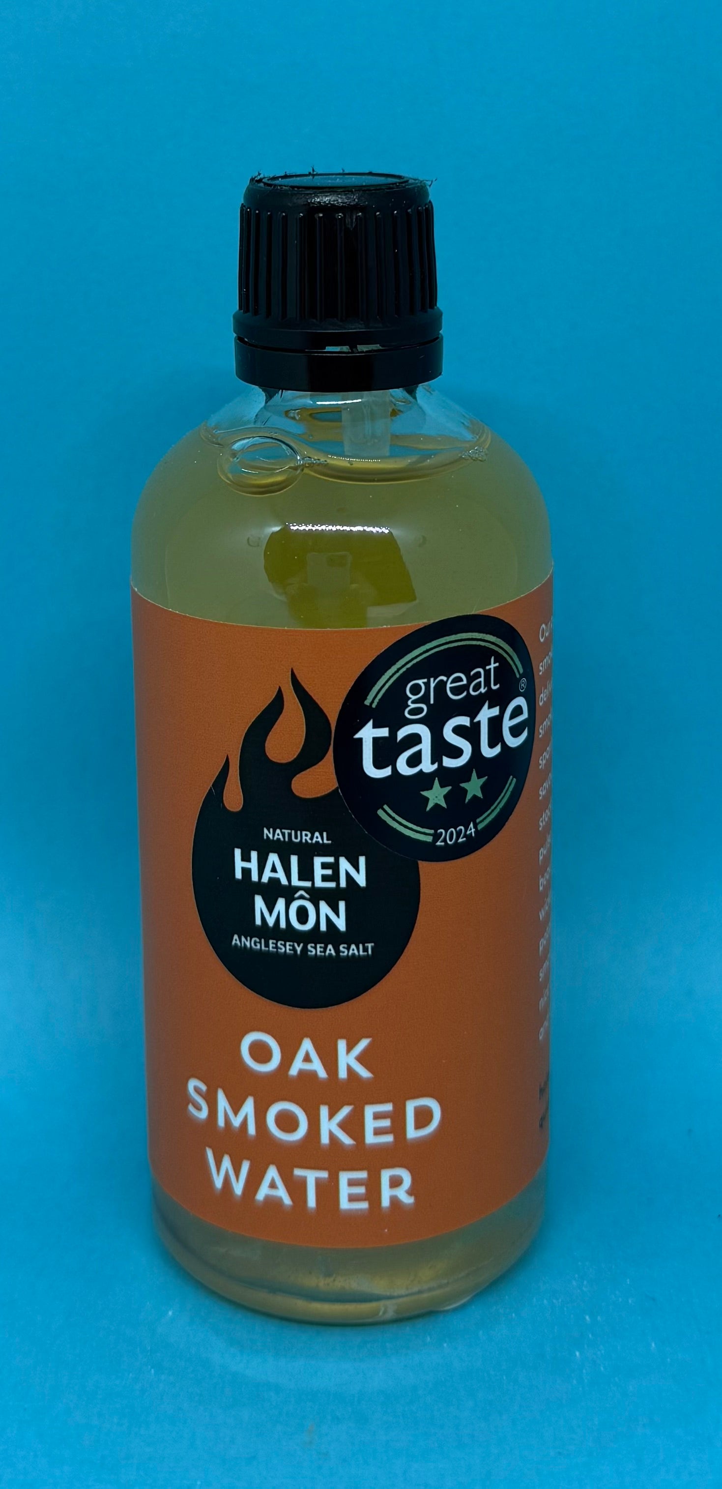 Bluebells and Thyme Bottle of Oak Smoked Water with Halen Mon label on a blue background
