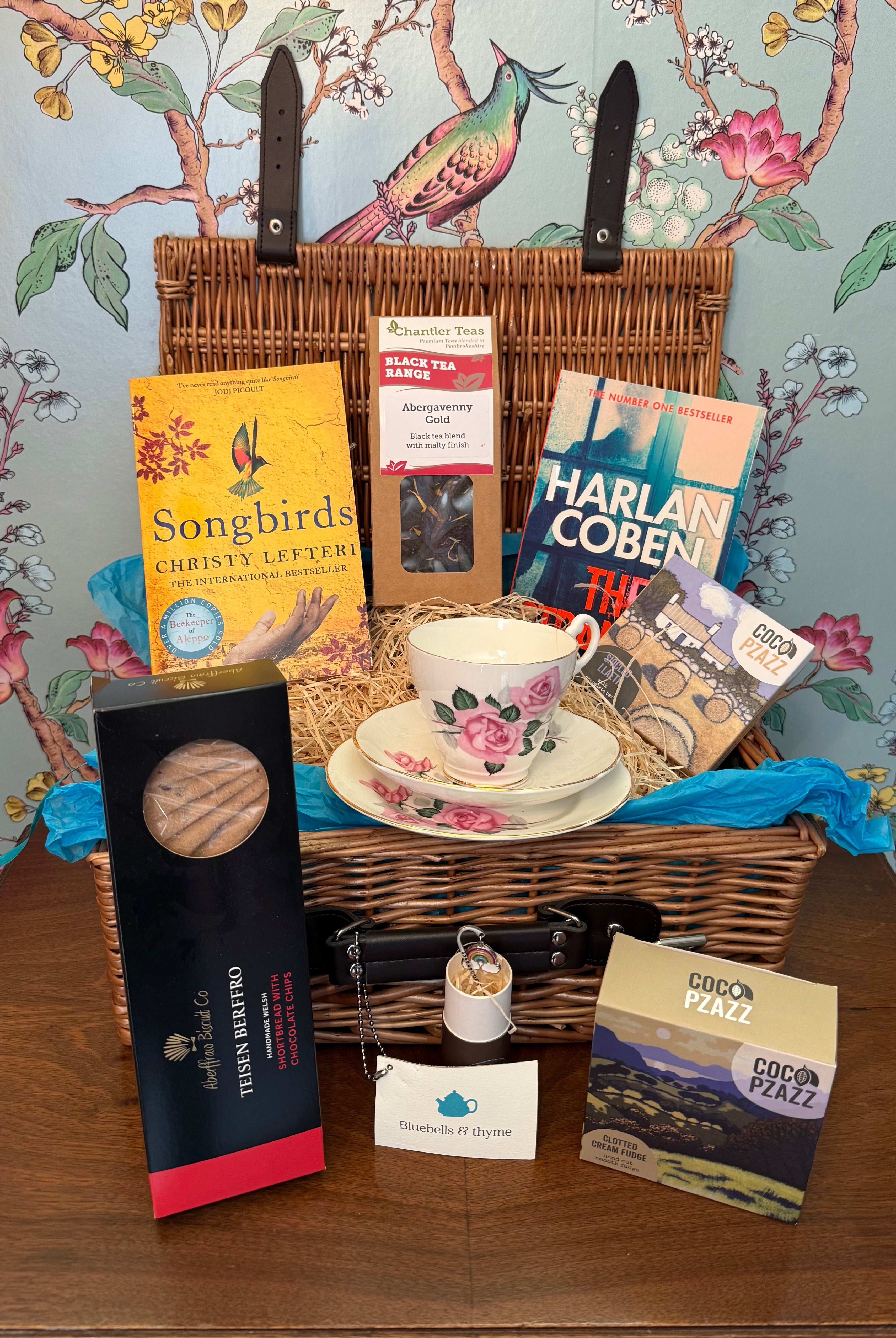 Bluebells & Thyme 'Tea & Tranquility' hamper, featuring vintage china and artisan foods, on an old cabinet.