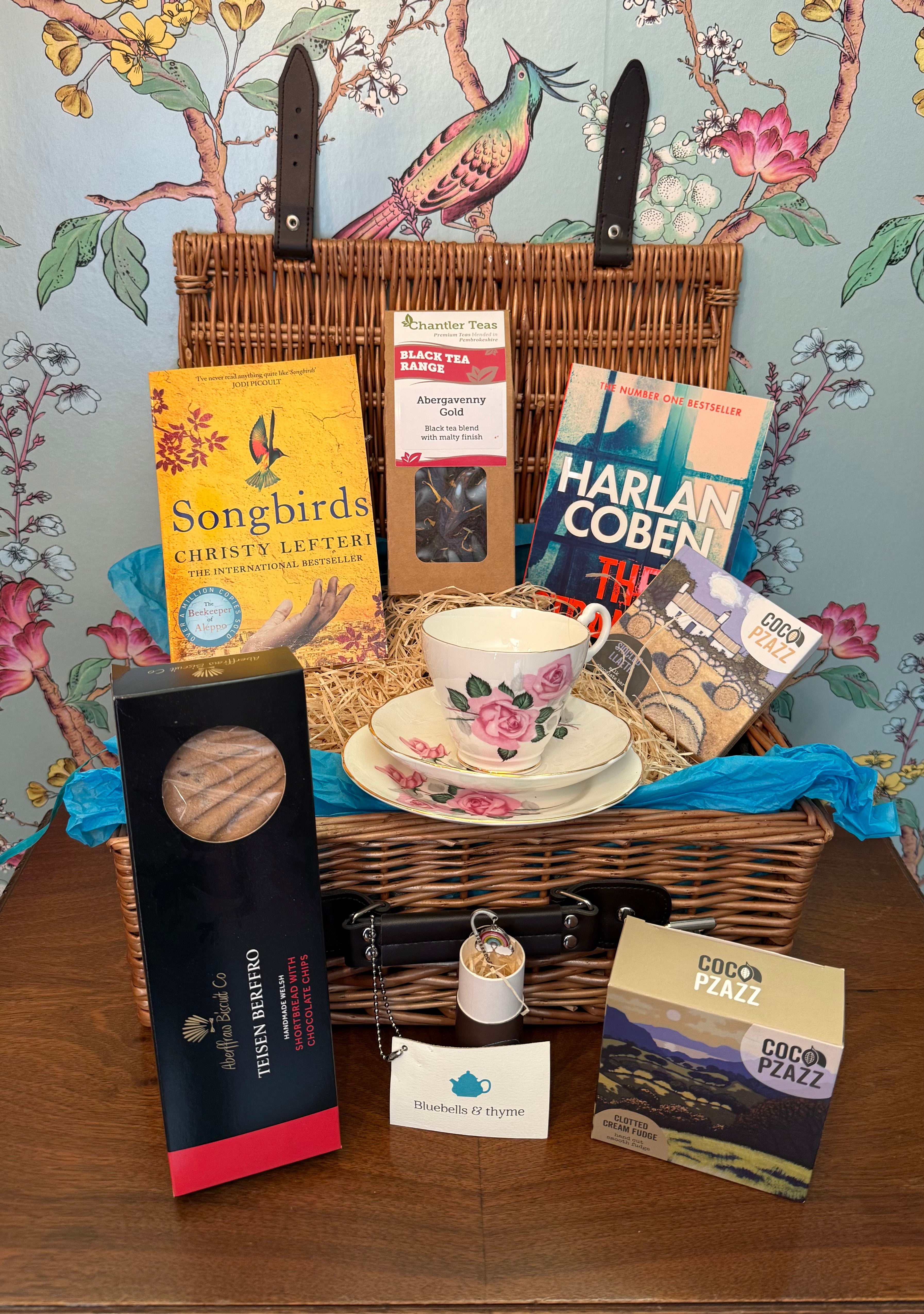Bluebells & Thyme 'Tea & Tranquility' hamper, featuring vintage china and artisan foods, on an old cabinet.