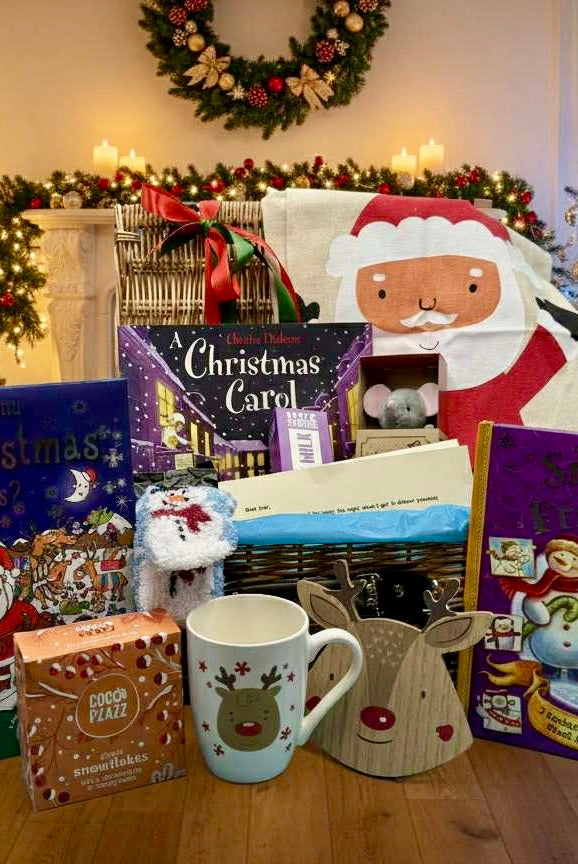 Bluebells and Thyme childrens Christmas eve box Collection of Christmas-themed books, a mug, and a Santa plush toy in a festive setting with Christmas trees and decorations.