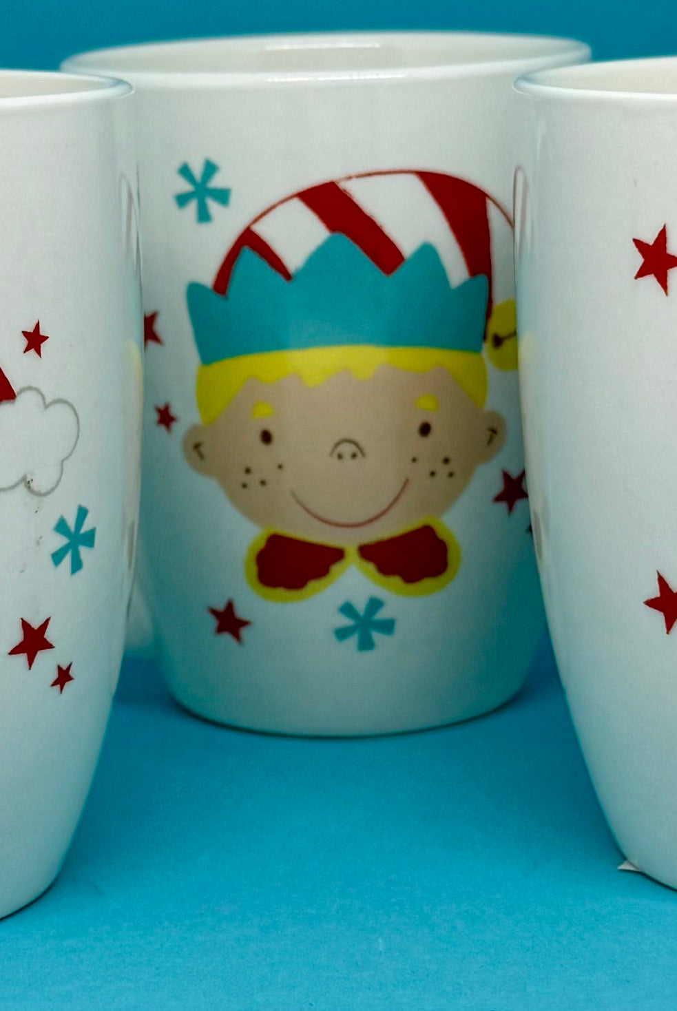 Three Christmas-themed mugs with Santa, a child, and a reindeer on a blue background