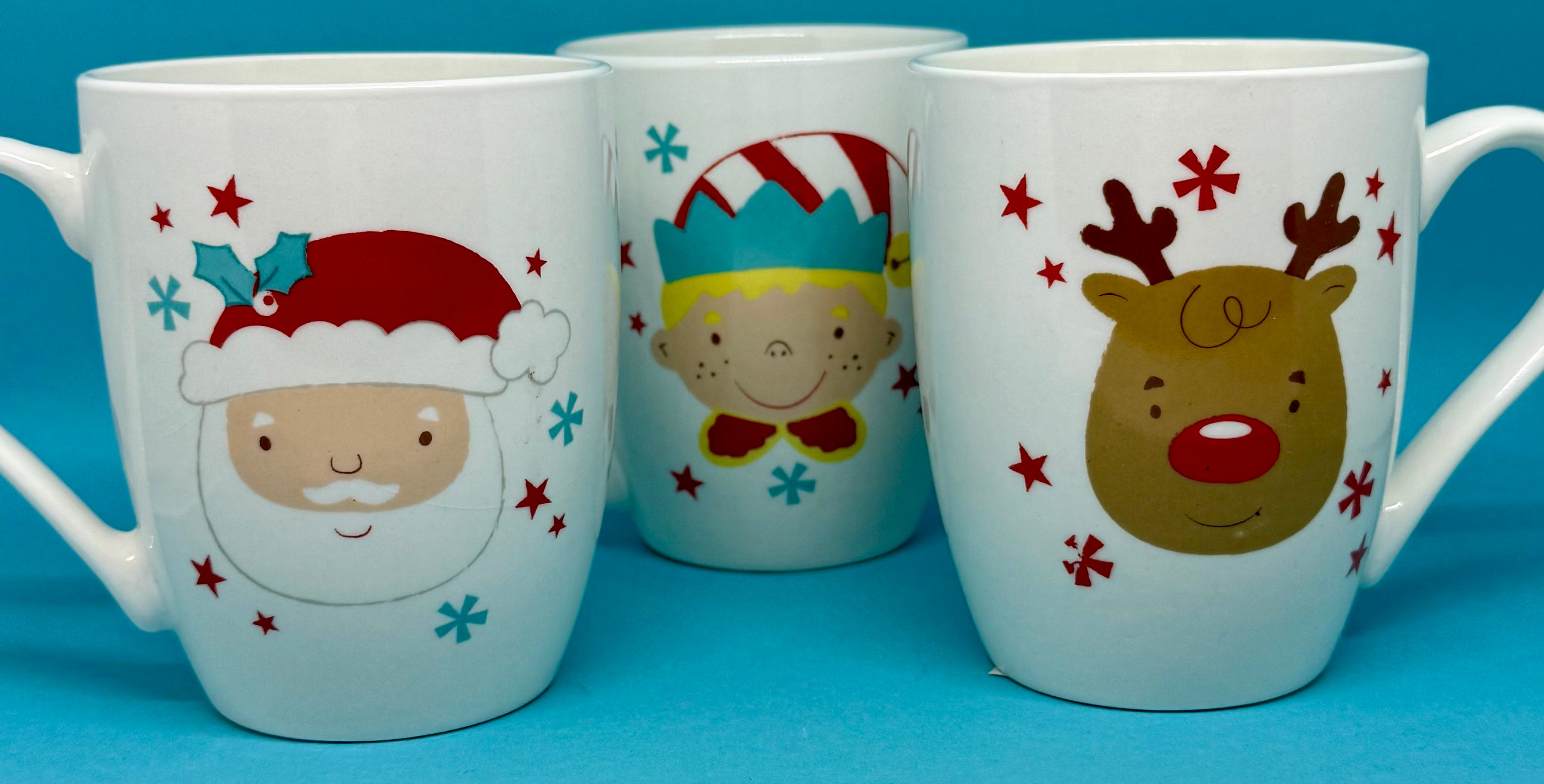 Three Christmas-themed mugs with Santa, a child, and a reindeer on a blue background