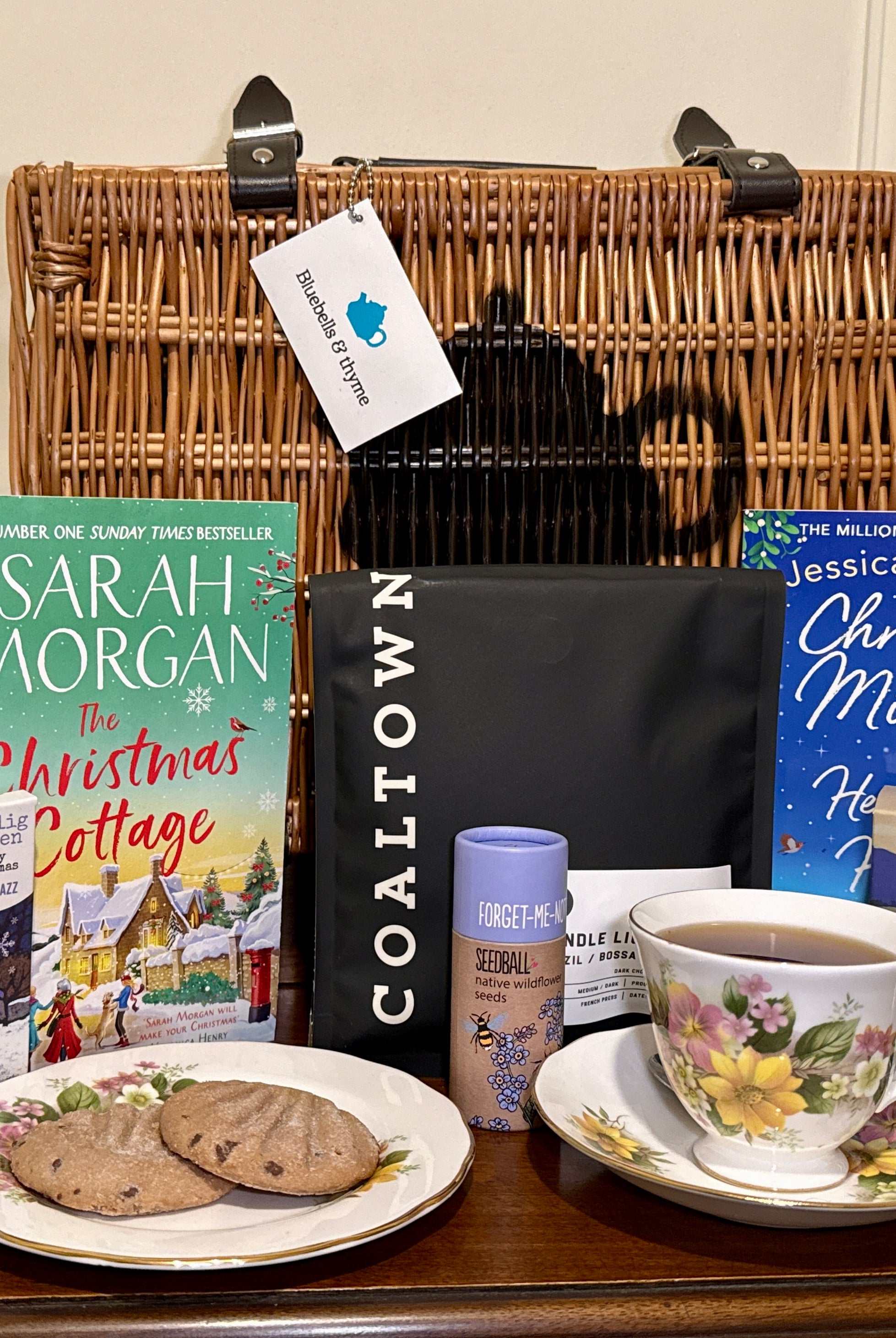 Bluebells and Thyme Wicker Hamper basket with books, a teacup, cookies, and a vintage china on a wooden surface.