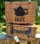Bluebells & Thyme branded wicker hampers, stacked outdoors in sunlight. Features the distinctive stencilled teapot logo.