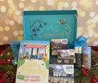 Christmas Gift box from bluebells and thyme with books, stationery items, and a small decorative sign on a festive background.