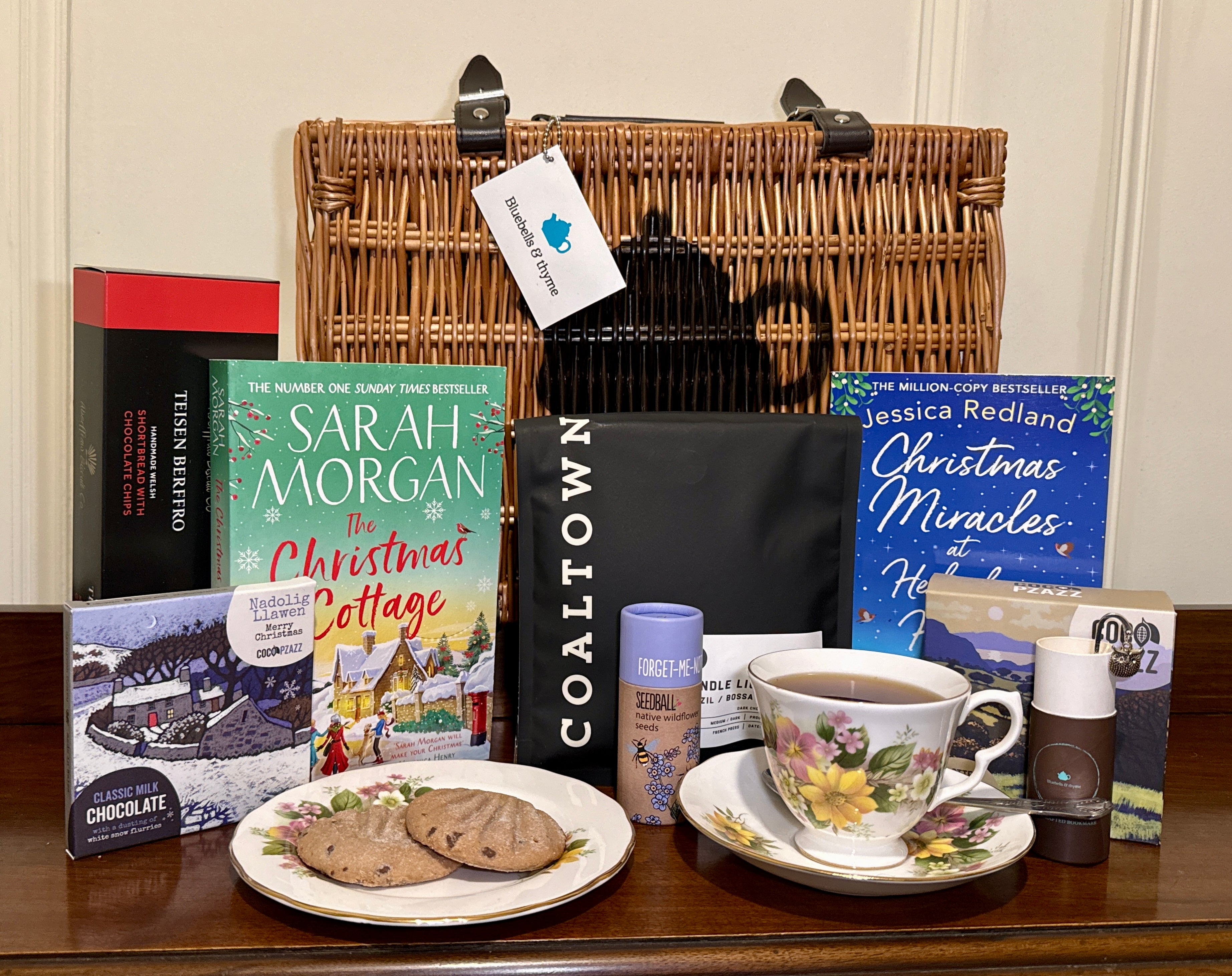 Bluebells and Thyme Wicker Hamper basket with books, a teacup, cookies, and a vintage china on a wooden surface.
