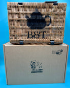 Bluebells and Thyme Wicker Hamper on top of a cardboard box with blue Christmas graphics on a blue background